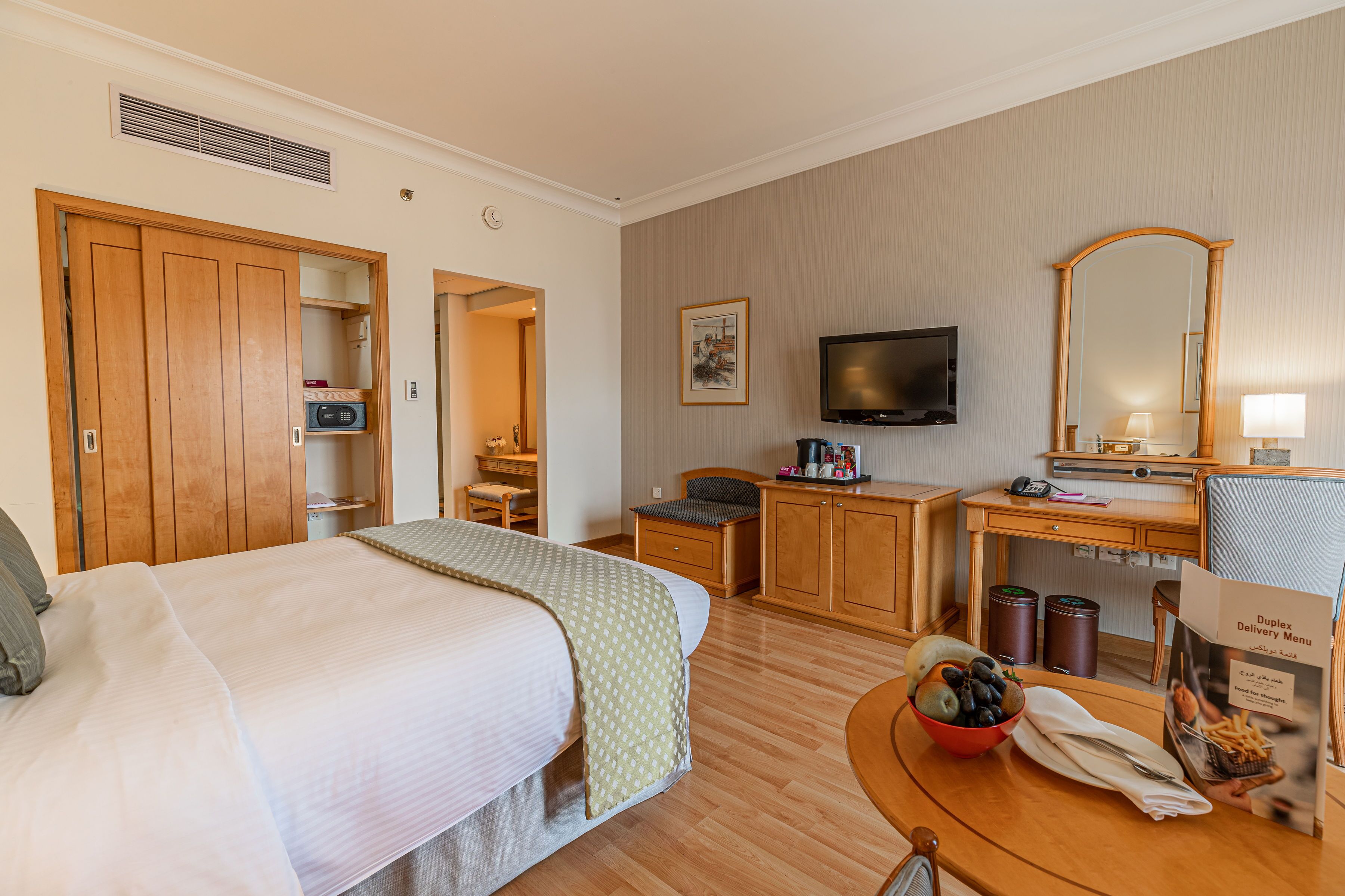 Ein Hotelzimmer mit Bett, Schreibtisch, Fernseher, Spiegel und einem kleinen Tisch mit Obstschale.