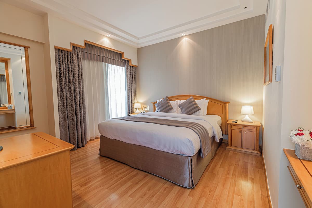 Een hotelkamer met een groot bed, houten hoofdbord, nachtkastjes met lampen, een spiegel en een houten dressoir.