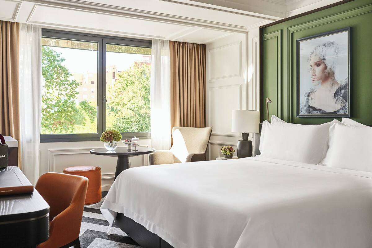 A hotel room with a large bed, a desk, a chair, and a view of the outdoors through a window.