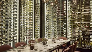 A dining area with a long table set for a meal, surrounded by wine racks filled with bottles. - Rosewood Villa Magna (Madrid)
