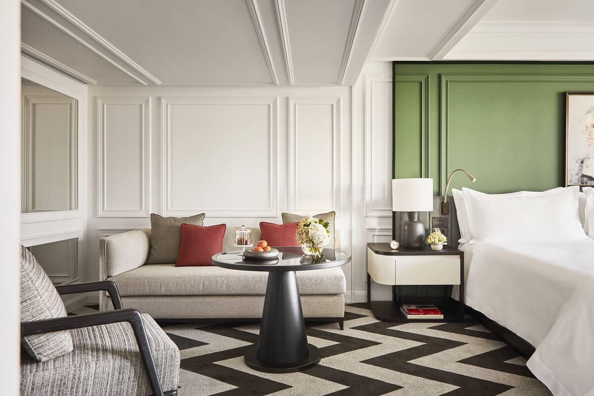 A hotel room with a bed, a sofa, a round coffee table, a nightstand, and a chair.