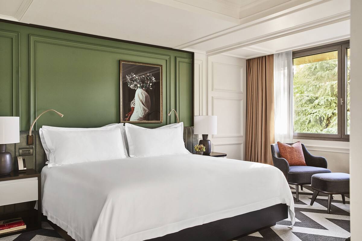 A hotel room with a large bed, a chair, a nightstand, and a window with curtains.