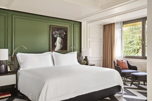 Ein Hotelzimmer mit einem großen Bett, einem Sessel, einem Nachttisch und einem Fenster mit Vorhängen.