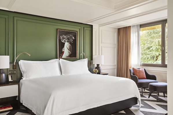 A hotel room with a large bed, a chair, a nightstand, and a window with curtains.