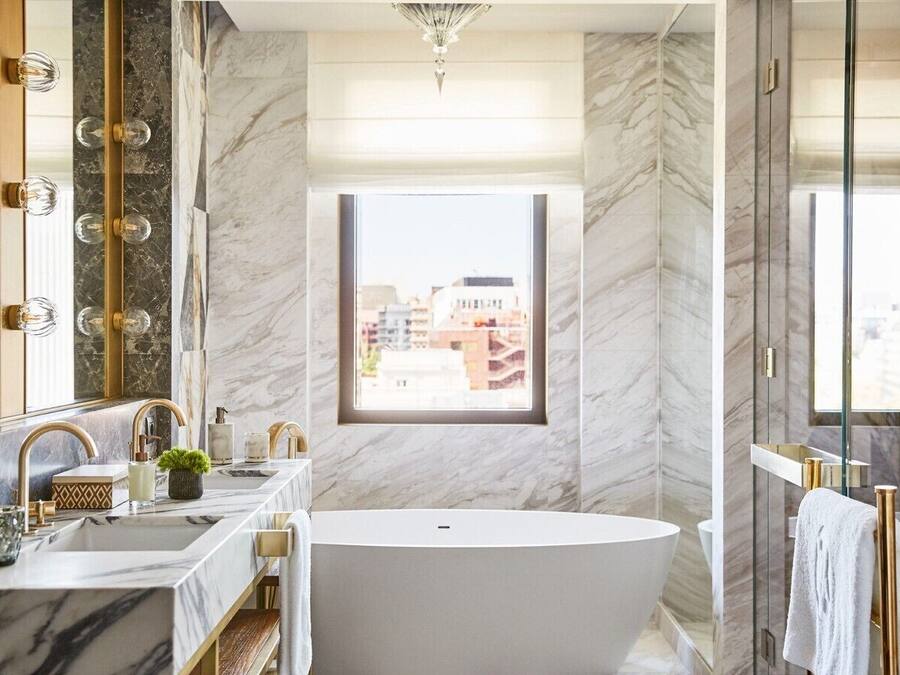 Un baño moderno con una bañera independiente, un espejo grande y una ventana que ofrece vistas a la ciudad.