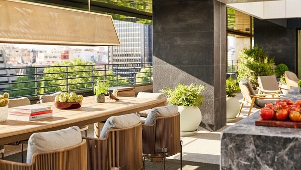 A modern outdoor dining area with wicker chairs, a wooden table, and potted plants. - Rosewood Villa Magna (Madrid)