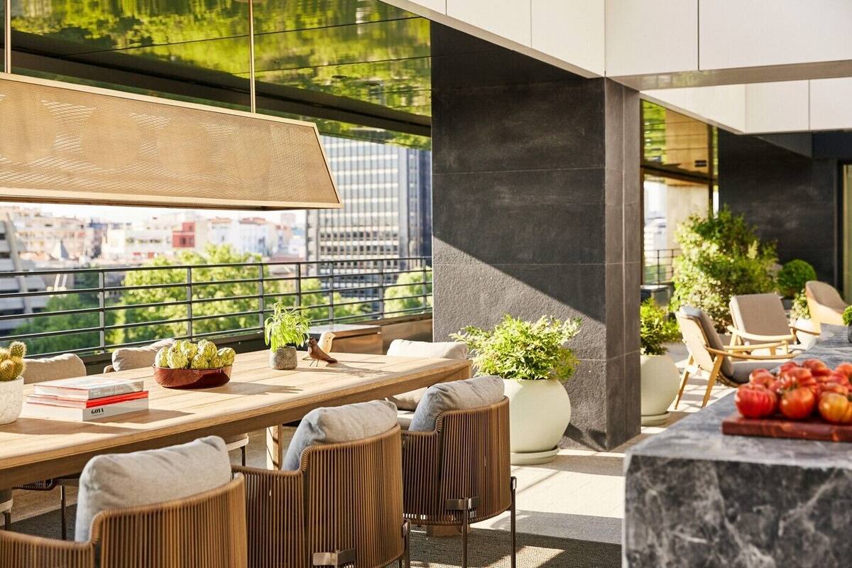 A modern outdoor dining area with wicker chairs, a wooden table, and potted plants.