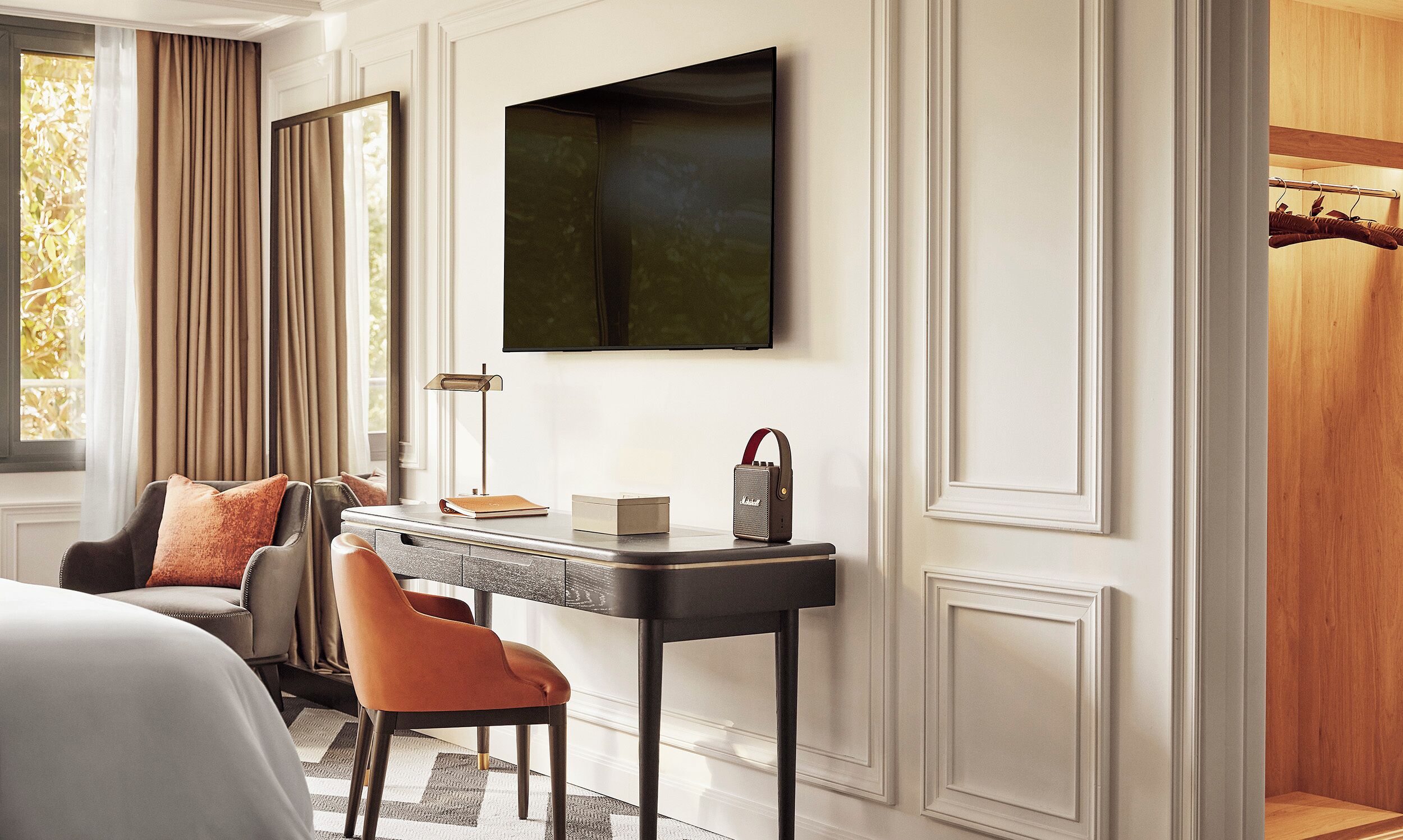 A modern hotel room with a bed, a desk with a lamp, a chair, and a television mounted on the wall.