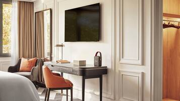 A modern hotel room with a bed, a desk with a lamp, a chair, and a television mounted on the wall.