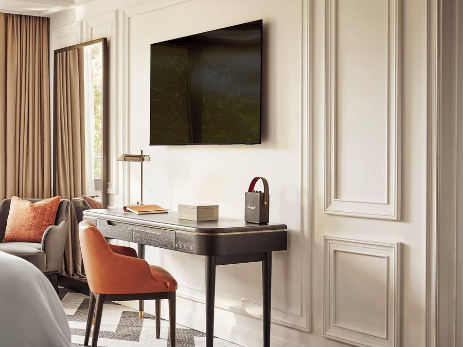 A modern hotel room with a bed, a desk with a lamp, a chair, and a television mounted on the wall.