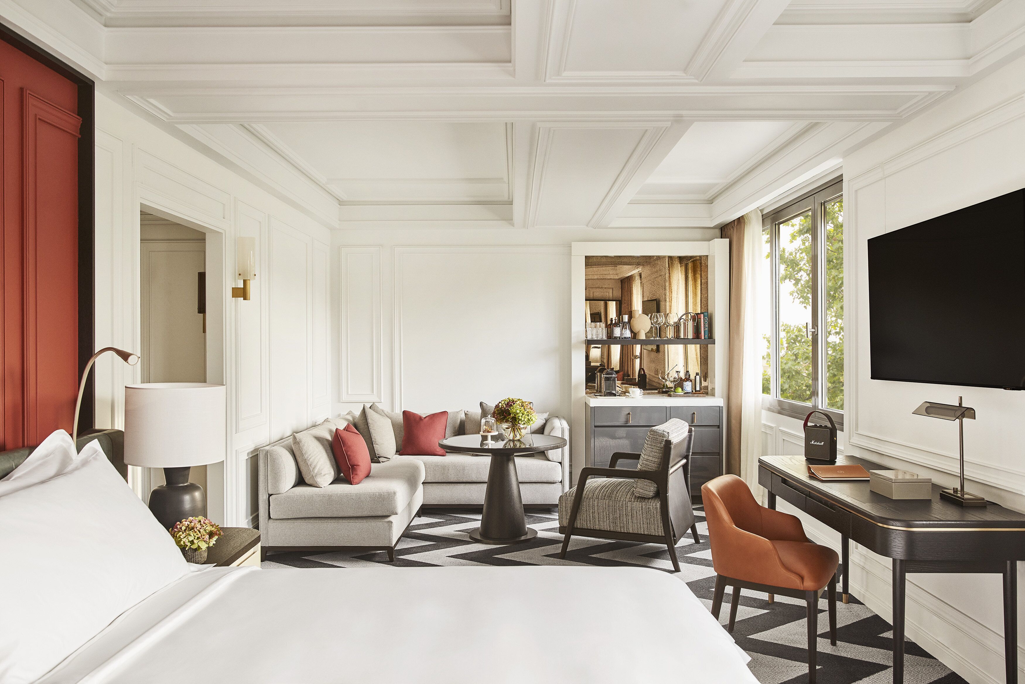 Quarto de hotel com cama, sofá, escrivaninha e área de refeições.