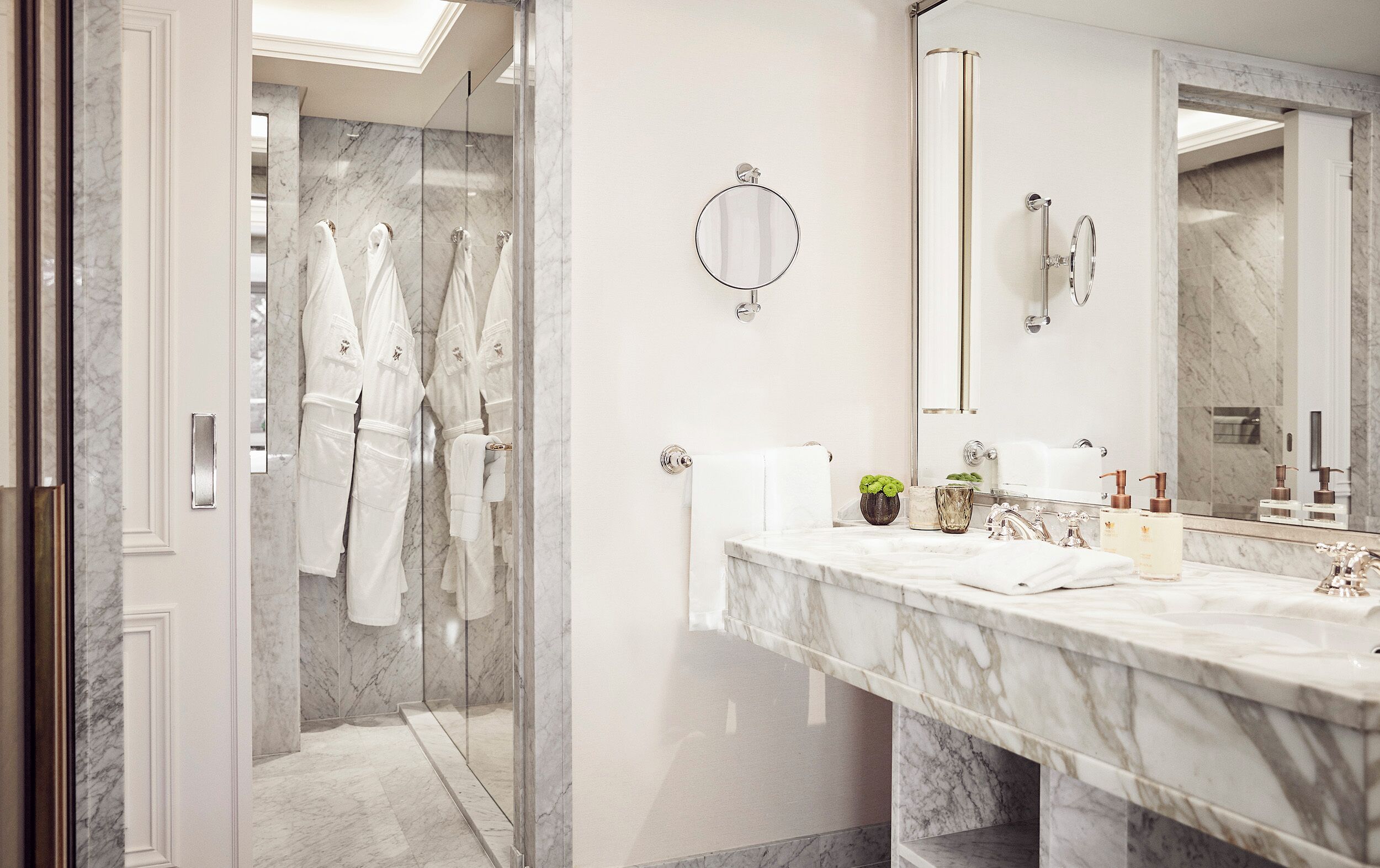 A modern bathroom with a glass shower enclosure, marble countertops, and a large mirror.