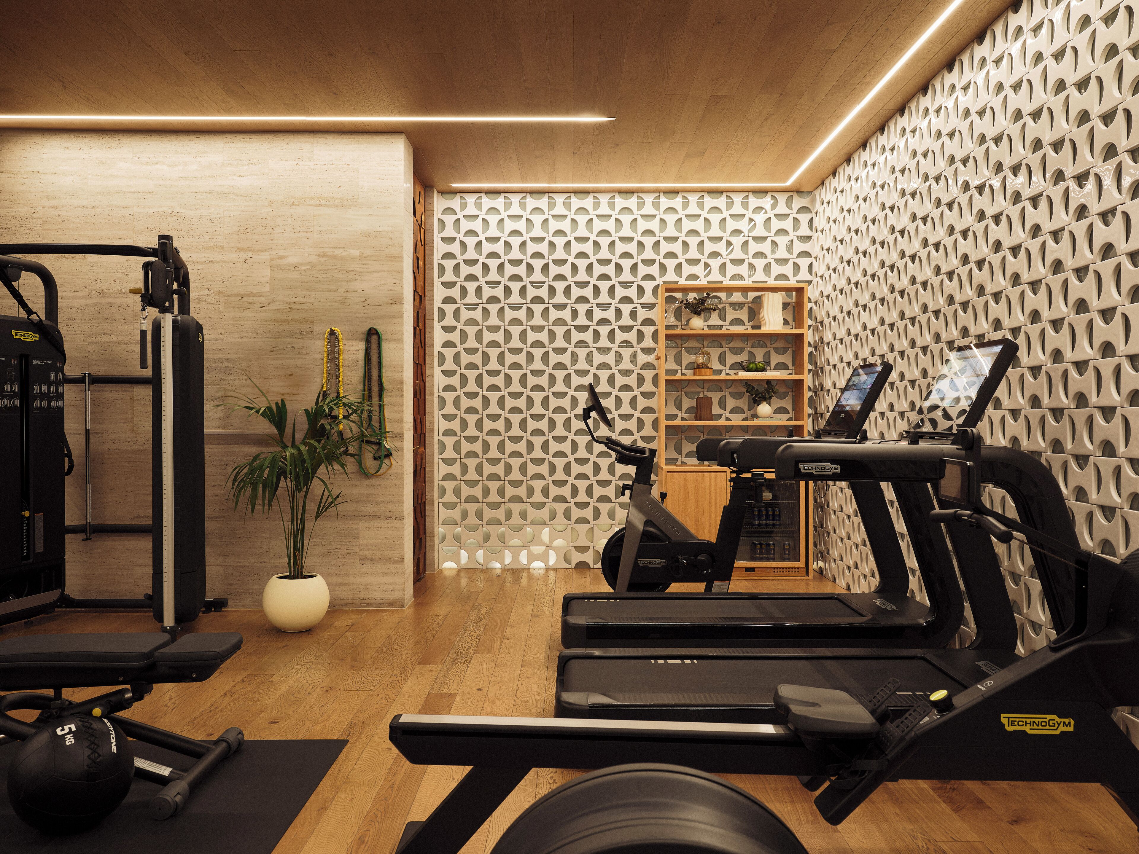 A gym with exercise equipment, a wooden floor, and a patterned wall.