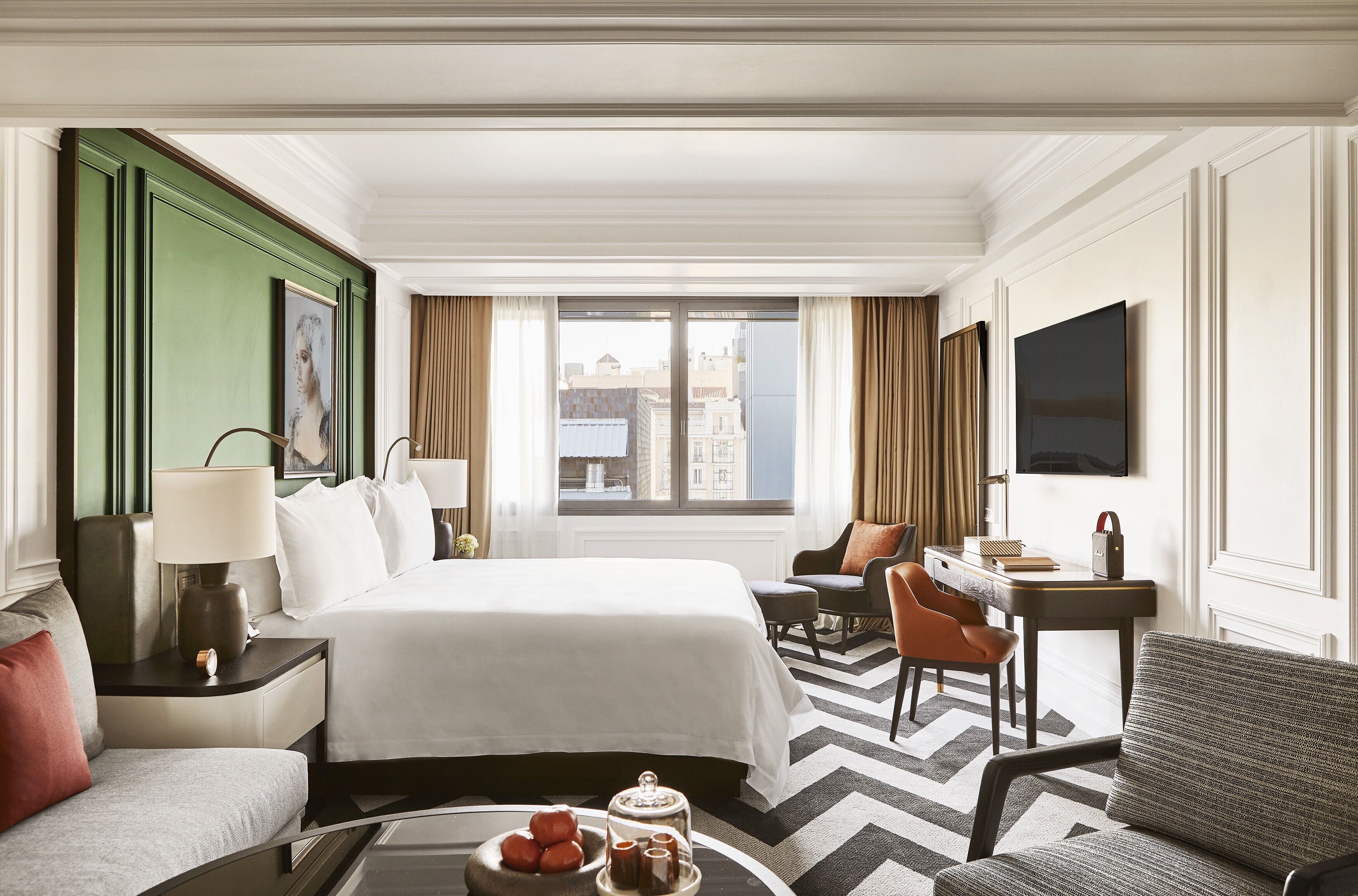 Ett hotellrum med en stor säng, ett skrivbord, en stol, en soffa och utsikt över staden.