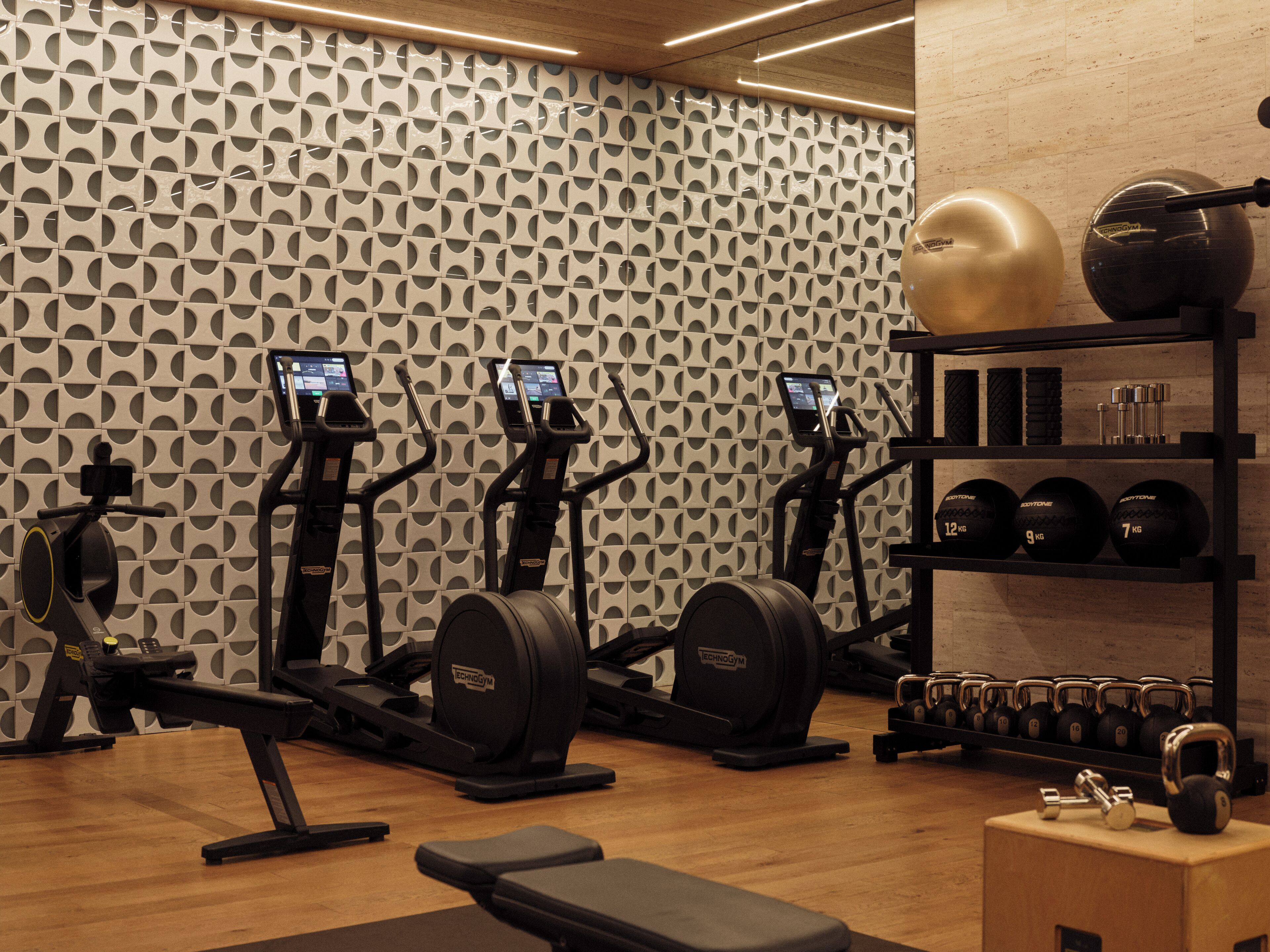Ein Fitnessraum mit Laufbändern, Crosstrainern, einer Bank, Kettlebells und Kurzhanteln.