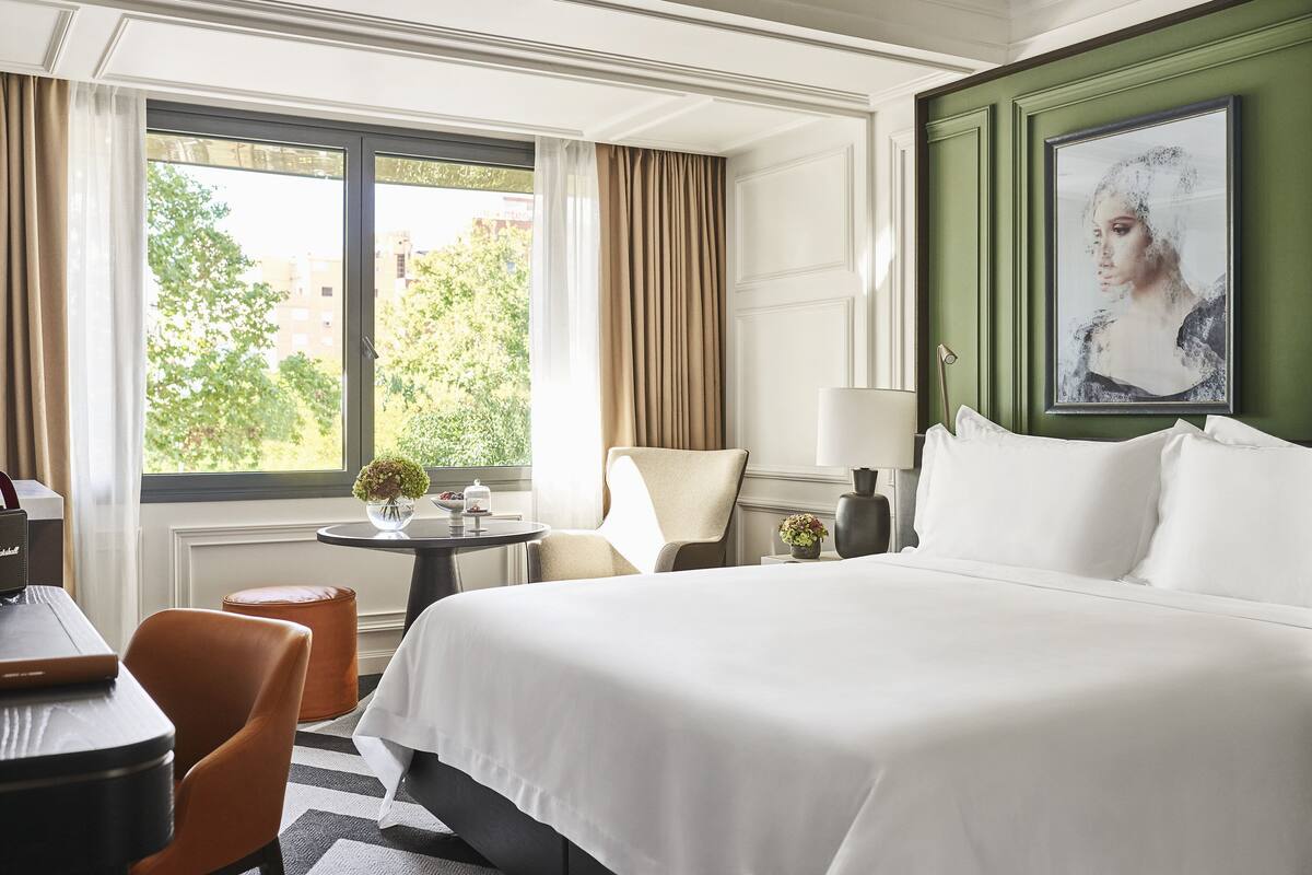 A hotel room with a large bed, a desk, a chair, and a view of the outdoors.
