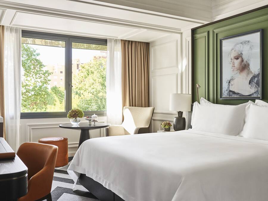 Habitación de hotel con una cama grande, un escritorio, una silla y vistas al exterior.