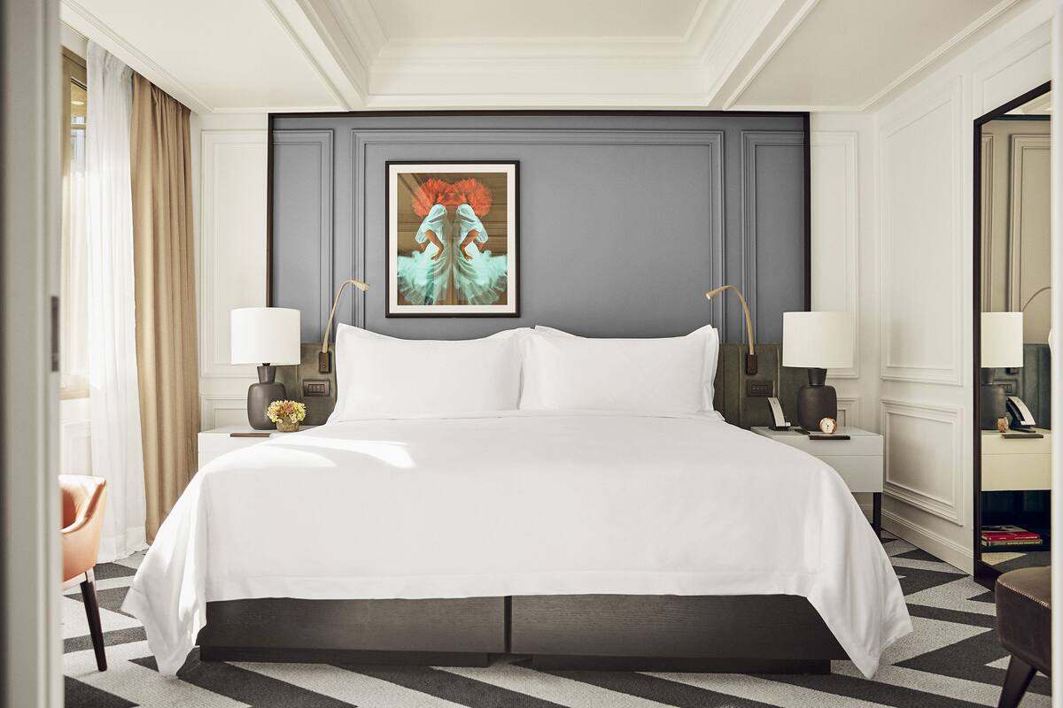 A hotel room with a large bed, two bedside tables with lamps, a framed artwork on the wall, and a mirror on the opposite wall.