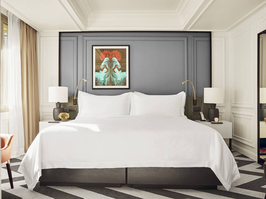 Hotelkamer met een groot bed, twee nachtkastjes met lampen, een lijst met kunstwerk aan de muur en een spiegel aan de overkant.