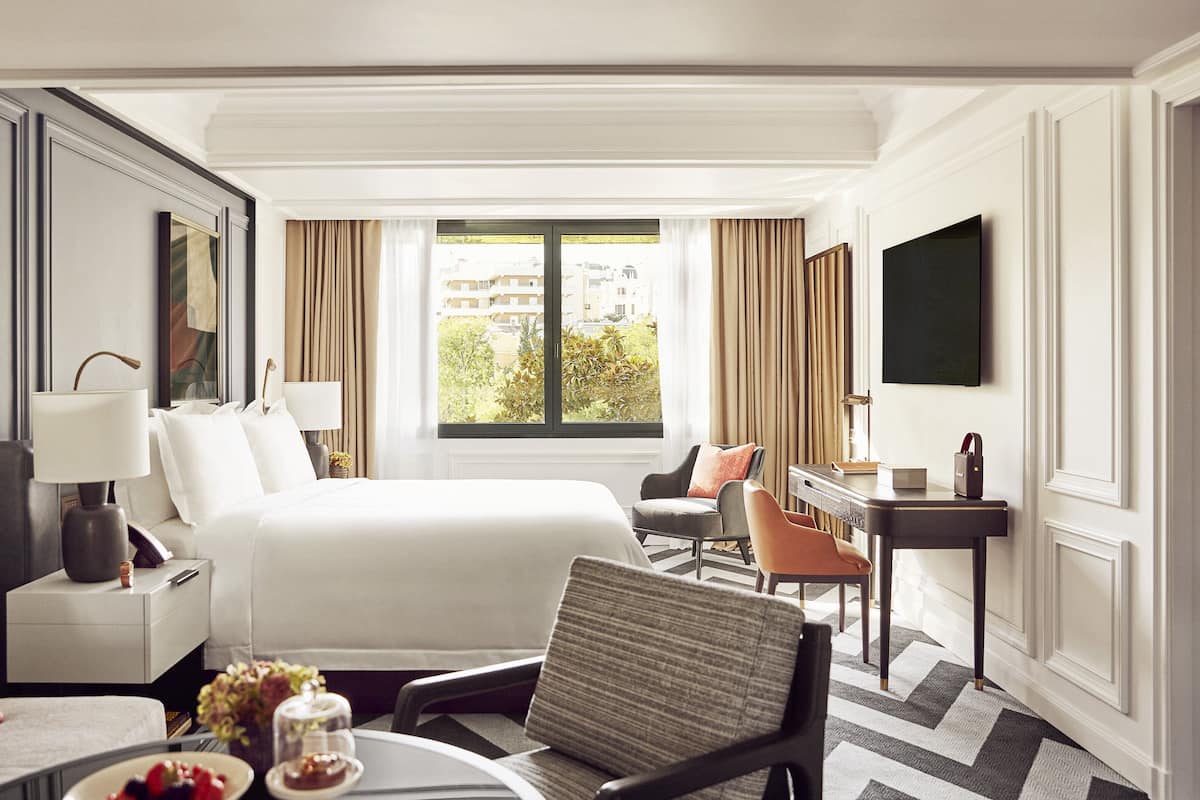 A hotel room with a large bed, a desk, a chair, a TV, and a window with curtains.
