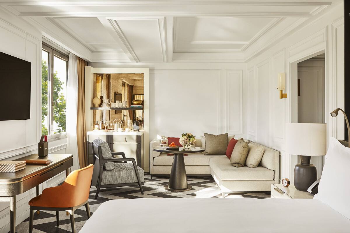 A hotel room with a bed, a desk, a chair, a sofa, a small table, and a TV.