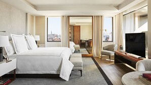A hotel room with a large bed, a TV, a desk, and a view of the city. - Rosewood Villa Magna (Madrid)