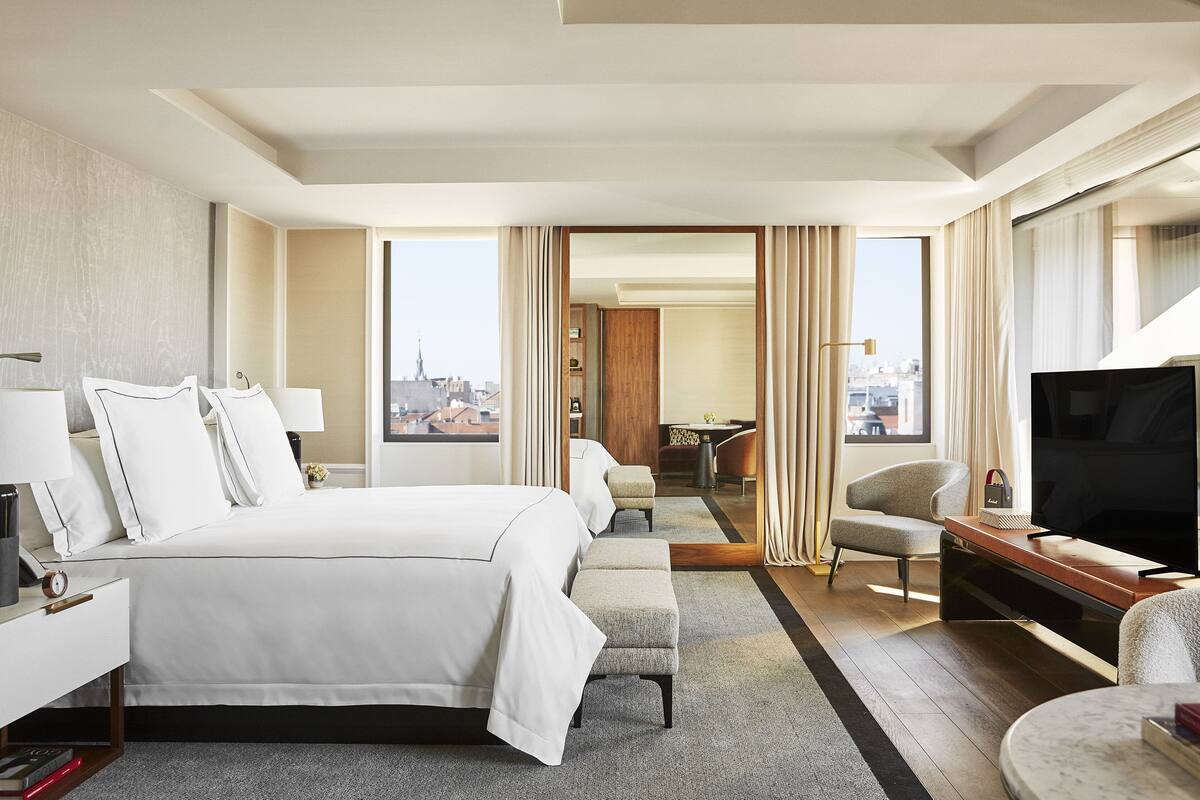 A hotel room with a large bed, a TV, a desk, and a view of the city.