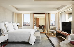 Ein Hotelzimmer mit einem großen Bett, einem Fernseher, einem Schreibtisch und Blick auf die Stadt.