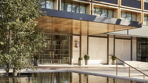 A modern building with a large glass facade, a reflective water feature, and a covered entrance area. - Rosewood Villa Magna (Madrid)