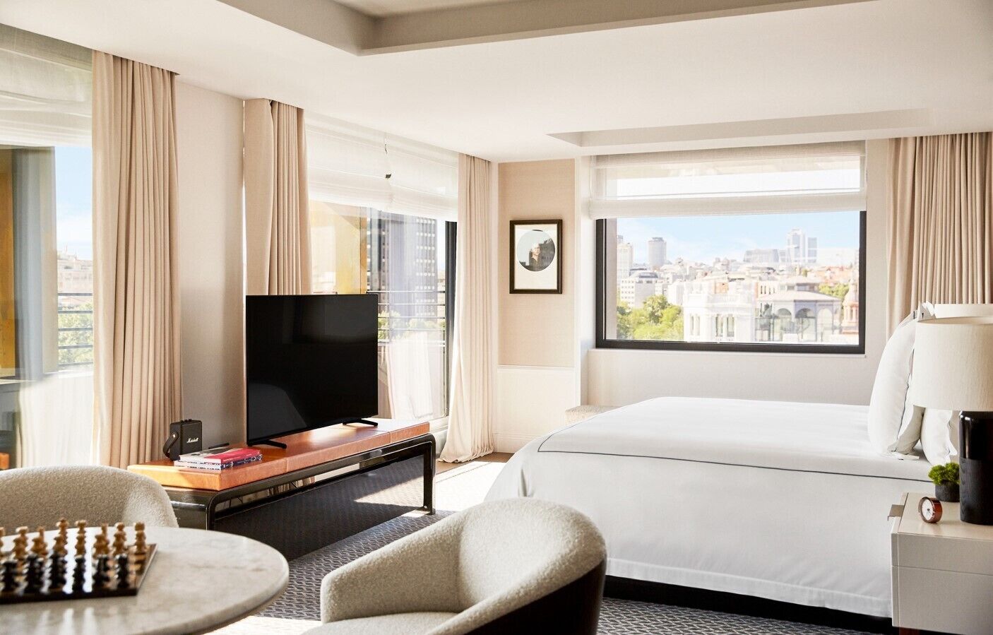 A hotel room with a large bed, a TV, a desk with a lamp, a chair, and a chessboard.