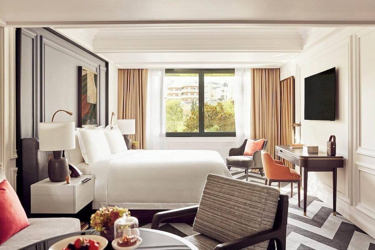 A hotel room with a bed, a desk, a chair, a TV, and a window with curtains.