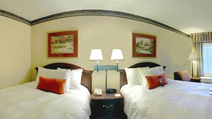 A hotel room with two beds, each with white bedding and red pillows. There are two wall-mounted lamps between the beds, and two framed paintings above each bed. - Hampton Inn Dalton (Dalton)