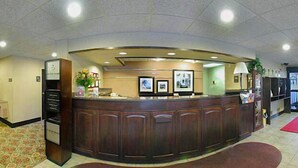 A reception area with a curved reception desk, a plant, framed pictures on the wall, and a red carpet leading to the entrance. - Hampton Inn Dalton (Dalton)