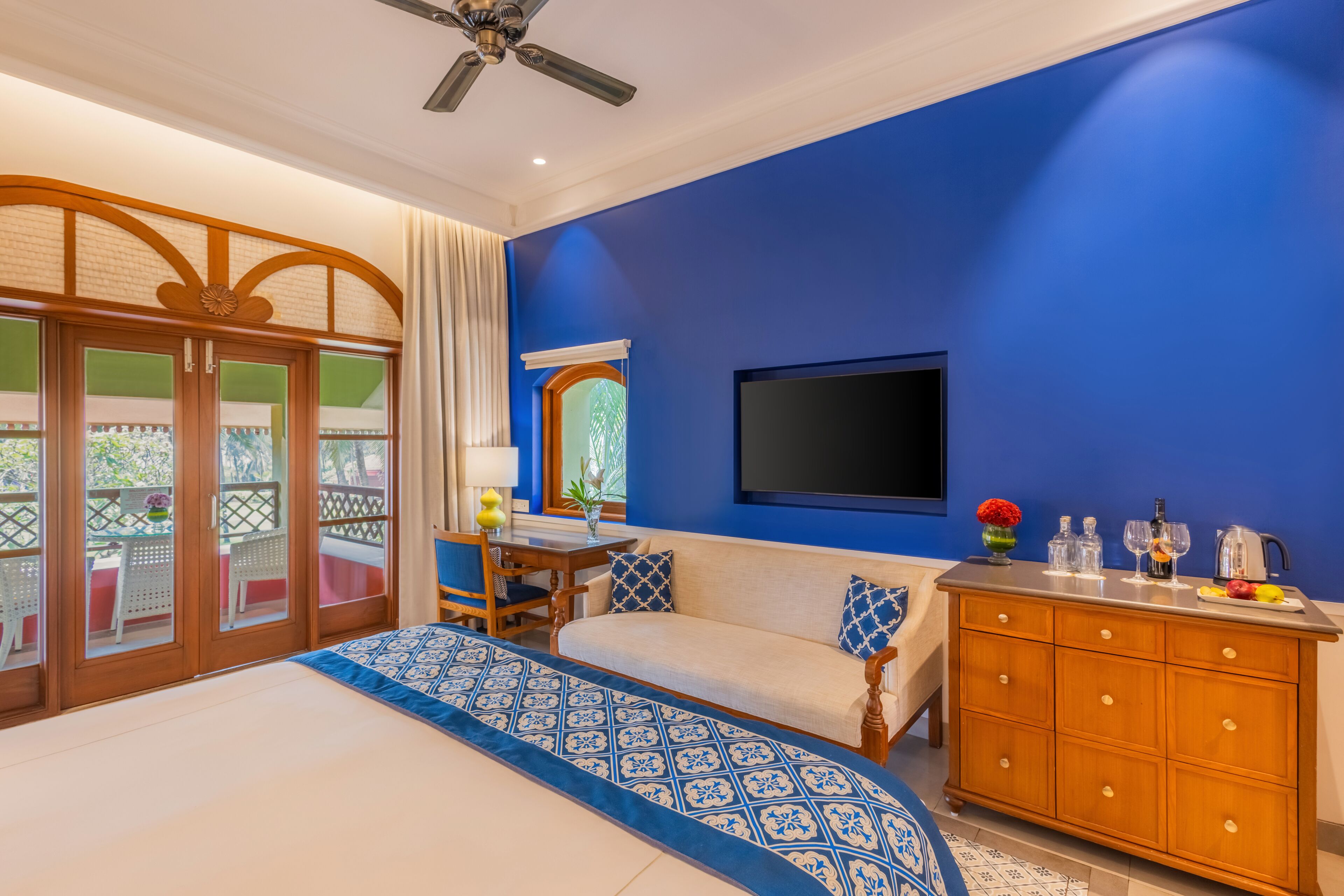 A bedroom with a bed, a sofa, a TV, a wooden cabinet, and a balcony with a view.