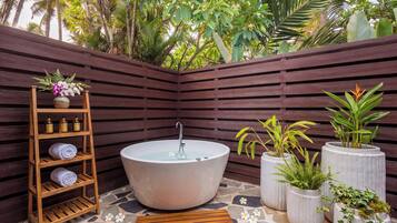 Un área de spa con una bañera independiente, estantes de madera con toallas y botellas, y plantas en macetas.