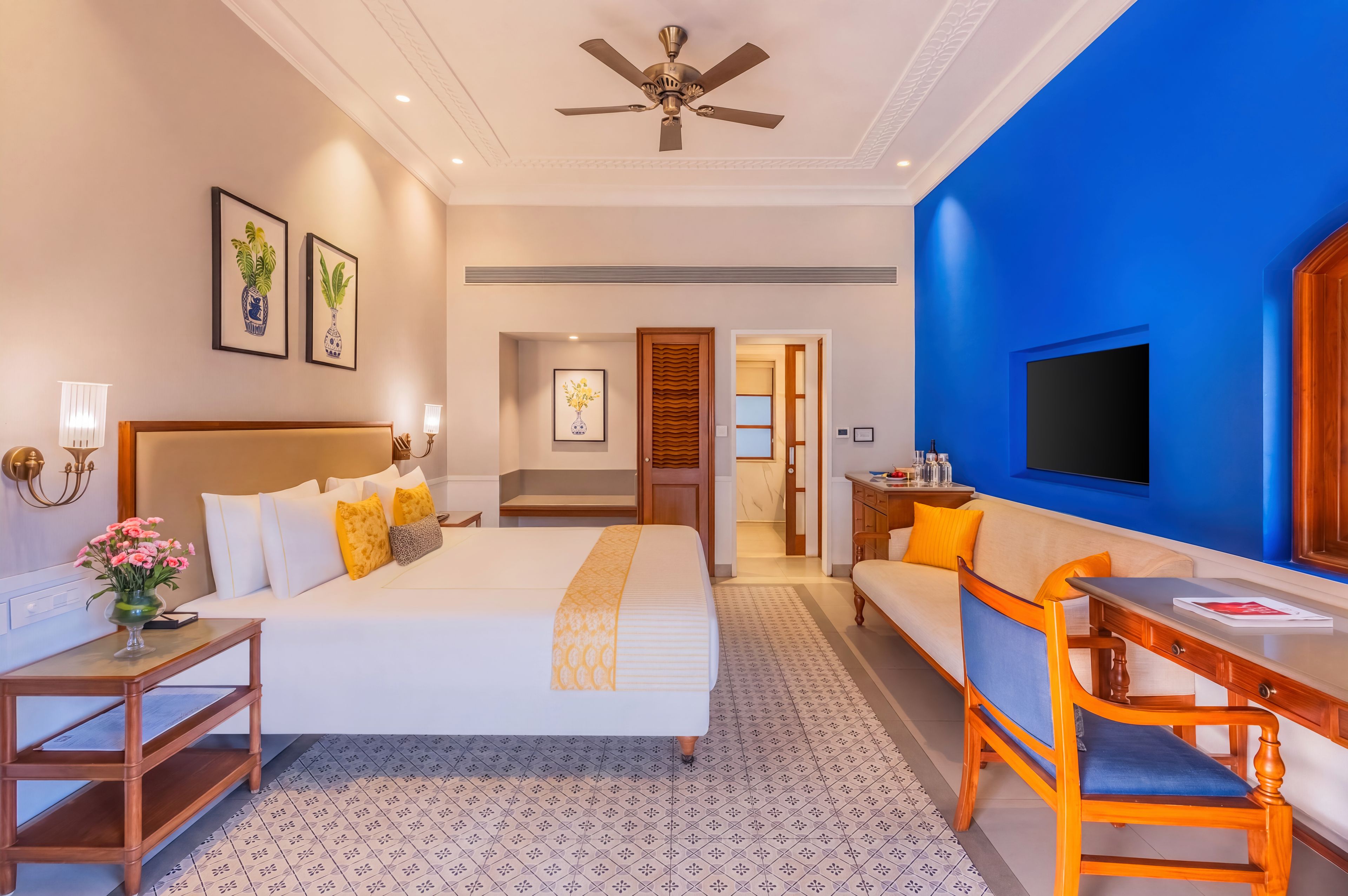A hotel room with a bed, a sofa, a TV, a desk, and a ceiling fan.