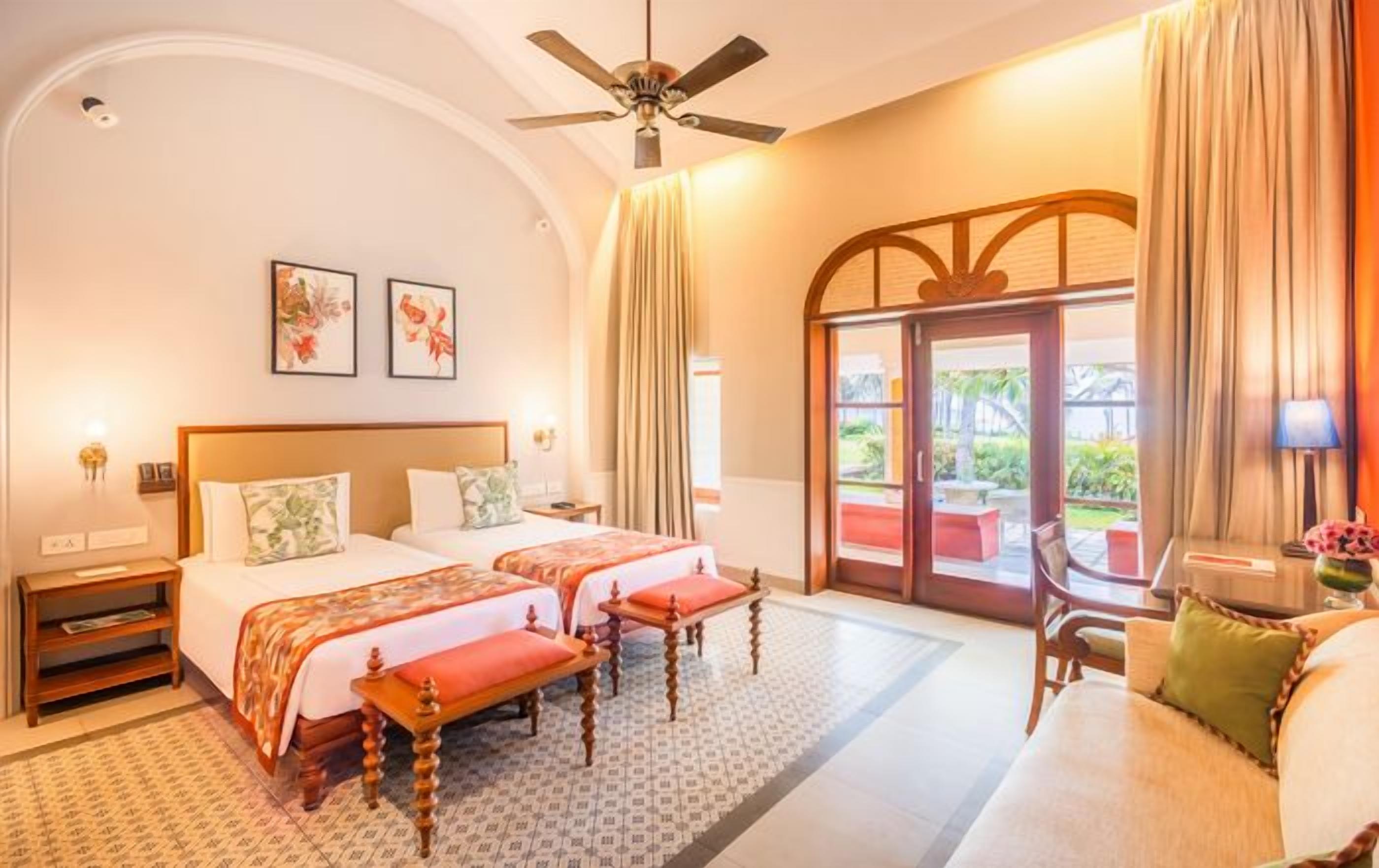 A hotel room with two beds, a ceiling fan, a sofa, and a view of the outdoors.