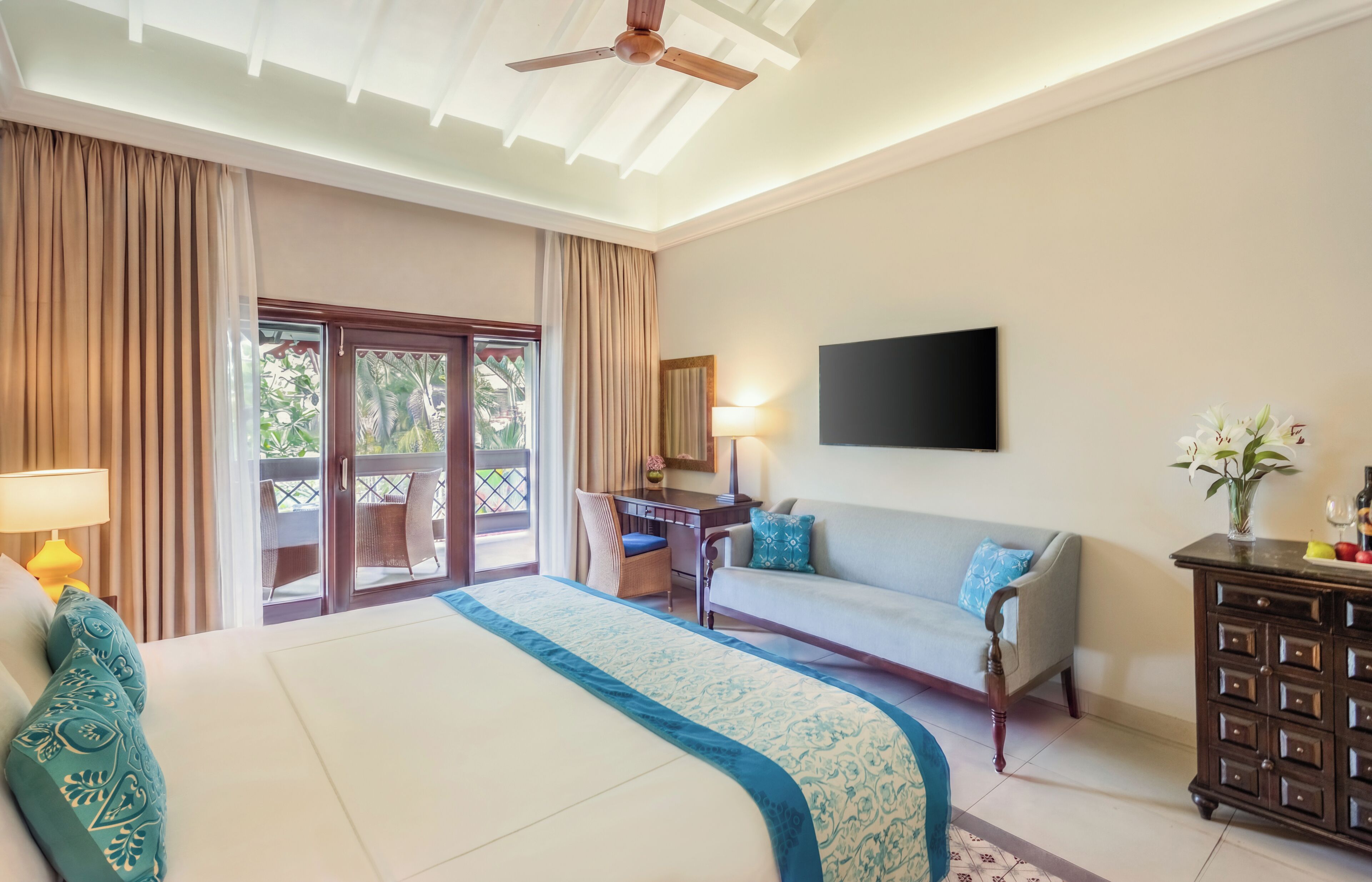 Quarto de hotel com uma cama grande, sofá, escrivaninha, televisão e vista para o exterior.