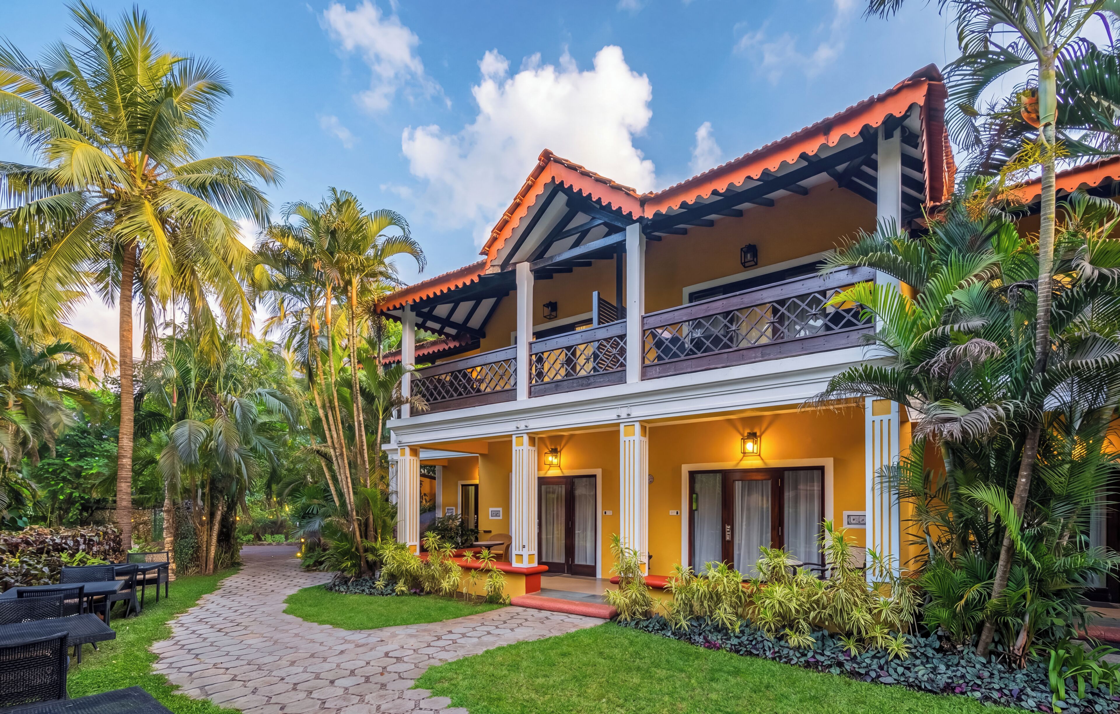 A two-story building with a balcony, surrounded by palm trees and a paved walkway.