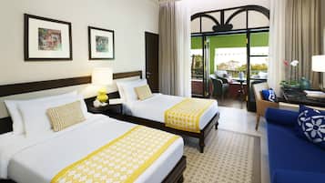 A hotel room with two beds, a sofa, a dining table, and a balcony with a view.