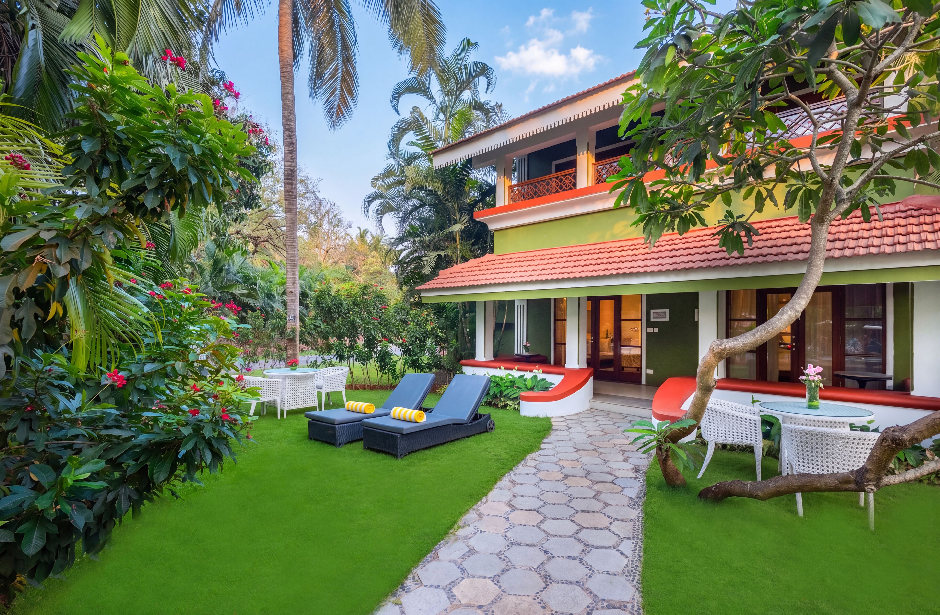 A two-story building with a red-tiled roof, a paved pathway, and outdoor seating with sun loungers.