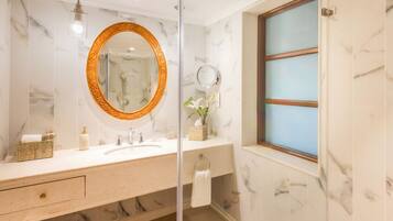 Un baño con pared de mármol, un espejo redondo con marco ornamentado, un lavabo y una ventana con vidrio esmerilado.