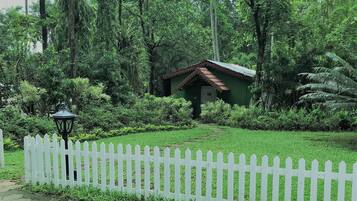 A small green building surrounded by lush greenery and a white picket fence.