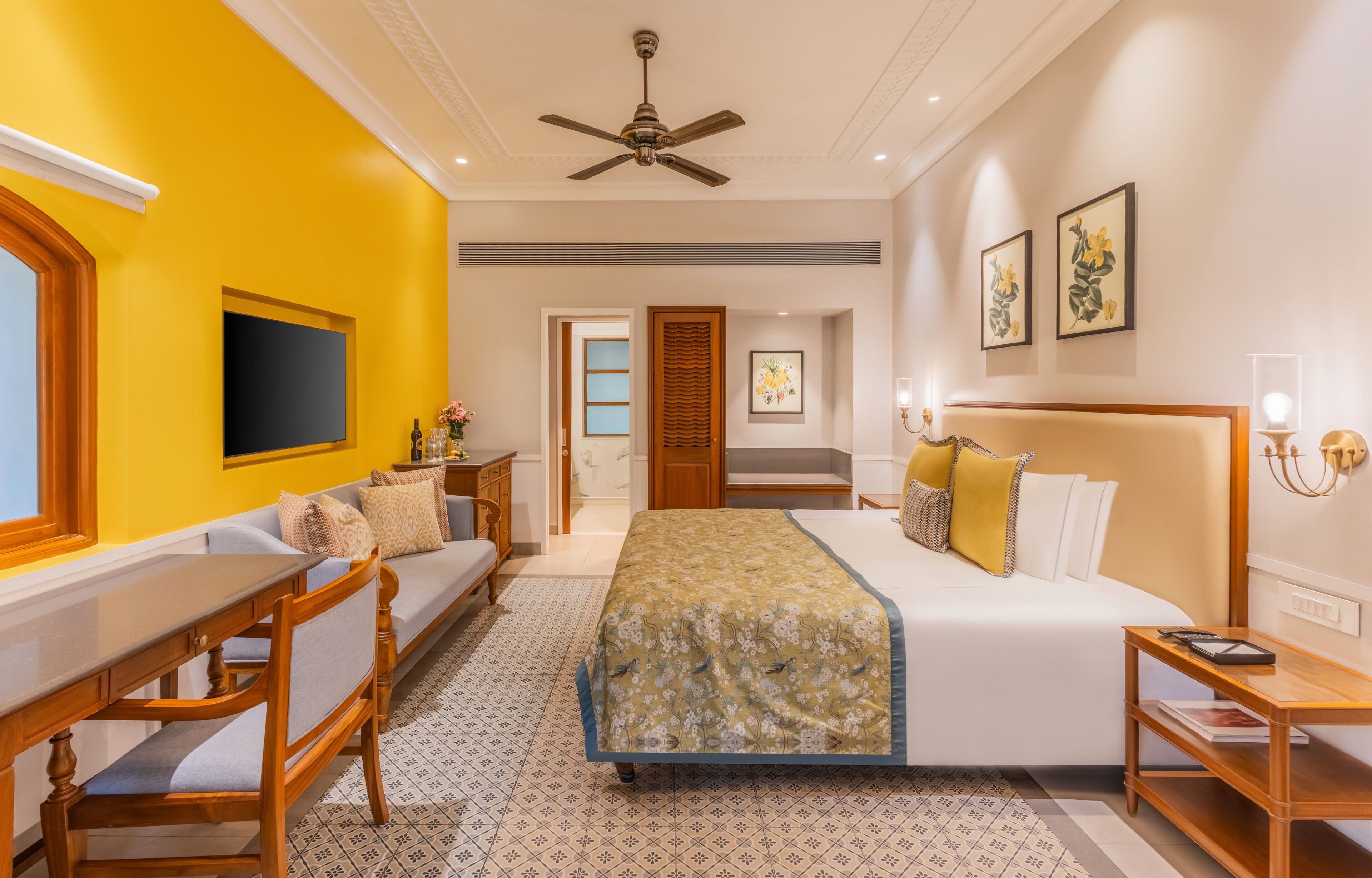A hotel room with a bed, a desk, a chair, a television, and a ceiling fan.