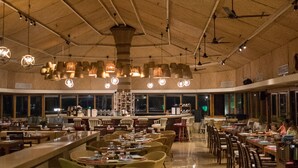 A spacious restaurant with high ceilings, multiple dining tables, wicker chairs, and hanging pendant lights. - Taj Holiday Village Resort & Spa (Candolim)