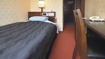 A hotel room with a bed, bedside table, lamp, chair, and a telephone.