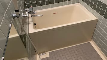 A bathroom with a rectangular bathtub, a handheld showerhead, and a wall-mounted faucet.
