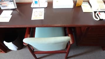 Een houten bureau met een stoel, een telefoon, een afstandsbediening en wat documenten.