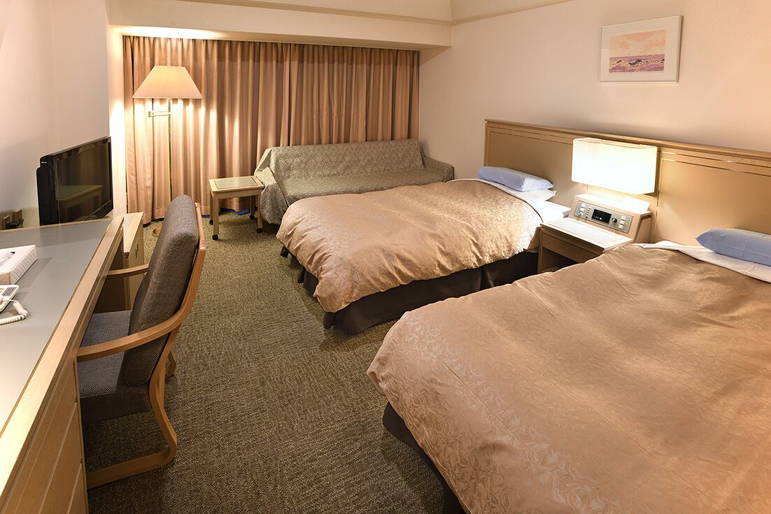 Ein Hotelzimmer mit Schreibtisch, zwei Betten, Fernseher, Lampe und einem fenster mit Vorhängen.