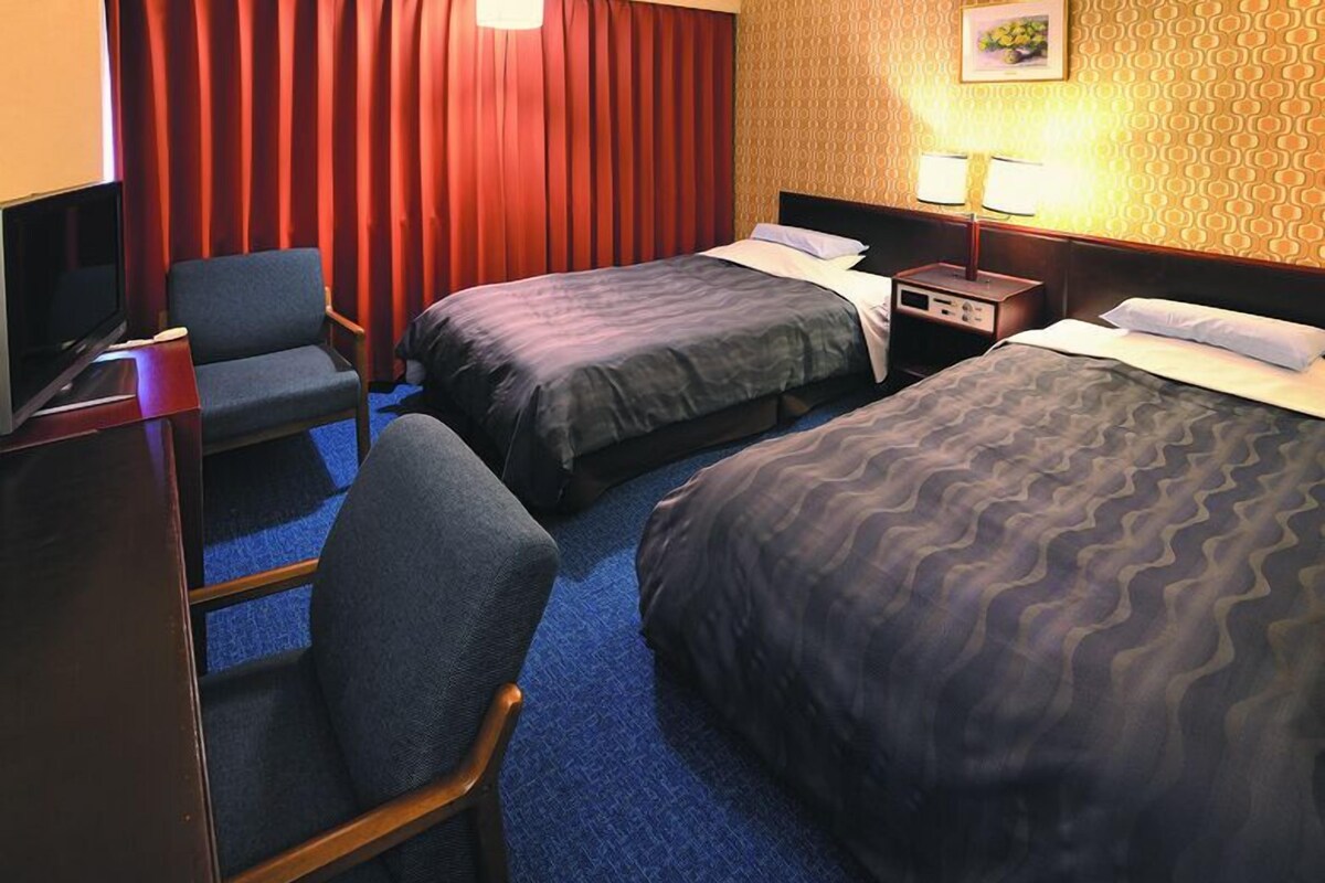 Habitación de hotel con dos camas, un escritorio, una silla, un televisor y una lámpara.